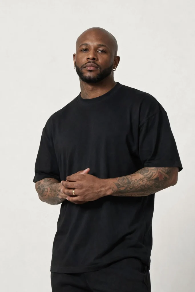 A studio portrait of a man wearing a black oversized T-shirt with a relaxed, clean silhouette. The minimalist design, solid color, and comfortable fit create a timeless streetwear essential suitable for everyday wear and modern casual collections.