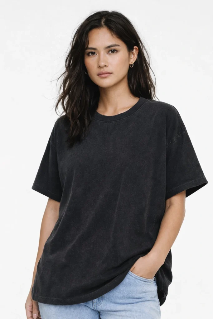 A clean studio portrait of a woman wearing a washed black oversized T-shirt paired with light denim. The relaxed silhouette and faded finish create a modern, effortless look suited for everyday wear and minimalist streetwear collections.