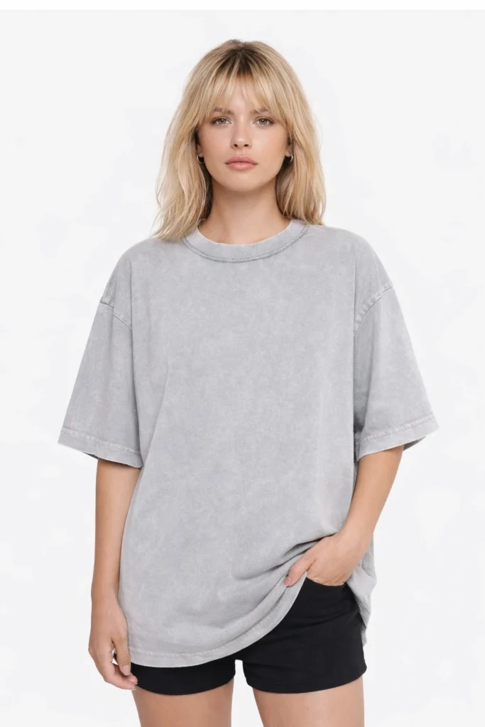 A clean studio portrait of a woman wearing a light gray washed oversized T-shirt paired with black shorts. The relaxed silhouette and soft washed finish create a modern, effortless look ideal for everyday wear and minimalist streetwear collections.