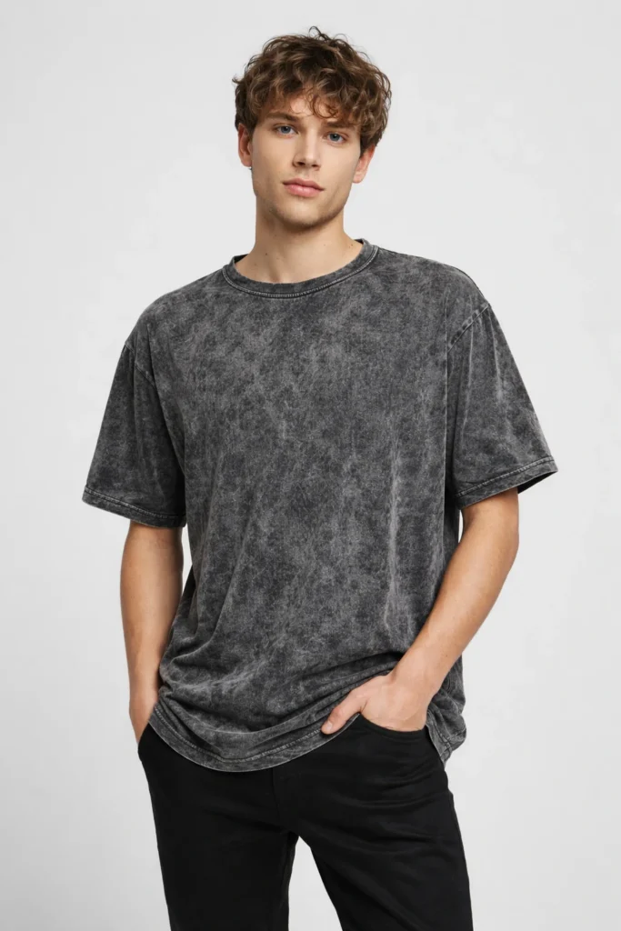 A studio portrait of a man wearing a washed charcoal oversized T-shirt paired with black pants. The stone-washed texture, relaxed silhouette, and muted tone create a modern vintage look ideal for everyday wear and contemporary streetwear collections.