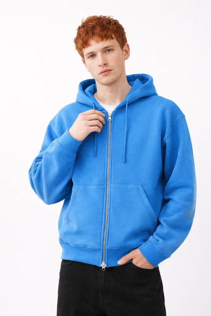 A clean studio image featuring a men’s blue zip-up hoodie with a relaxed fit and minimalist design. Styled with a full-length metal zipper, adjustable drawstring hood, ribbed cuffs, and front kangaroo pockets, this hoodie delivers a modern yet versatile look. Perfect for casualwear, streetwear collections, and private label hoodie manufacturing focused on comfort, color impact, and everyday wearability.