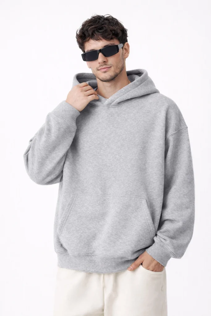 A studio-style image showcasing a men’s grey pullover hoodie with a relaxed, oversized fit and clean streetwear aesthetic. Designed with a classic hood, ribbed cuffs and hem, and a front kangaroo pocket, this hoodie delivers everyday comfort and modern versatility. Ideal for casualwear, streetwear collections, and private label hoodie manufacturing focused on neutral tones, soft fleece feel, and timeless silhouettes.