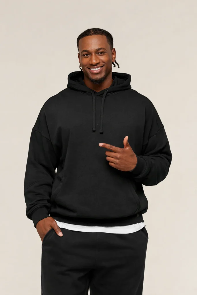 A modern lifestyle image showcasing a men’s black oversized pullover hoodie with a clean, minimal design. Crafted from soft fleece fabric, the hoodie features dropped shoulders, ribbed cuffs and hem, and a classic kangaroo pocket for everyday comfort. The relaxed silhouette paired with a neutral studio background highlights the hoodie’s versatility, making it ideal for casual wear, streetwear collections, and private label hoodie programs focused on comfort, simplicity, and contemporary style.