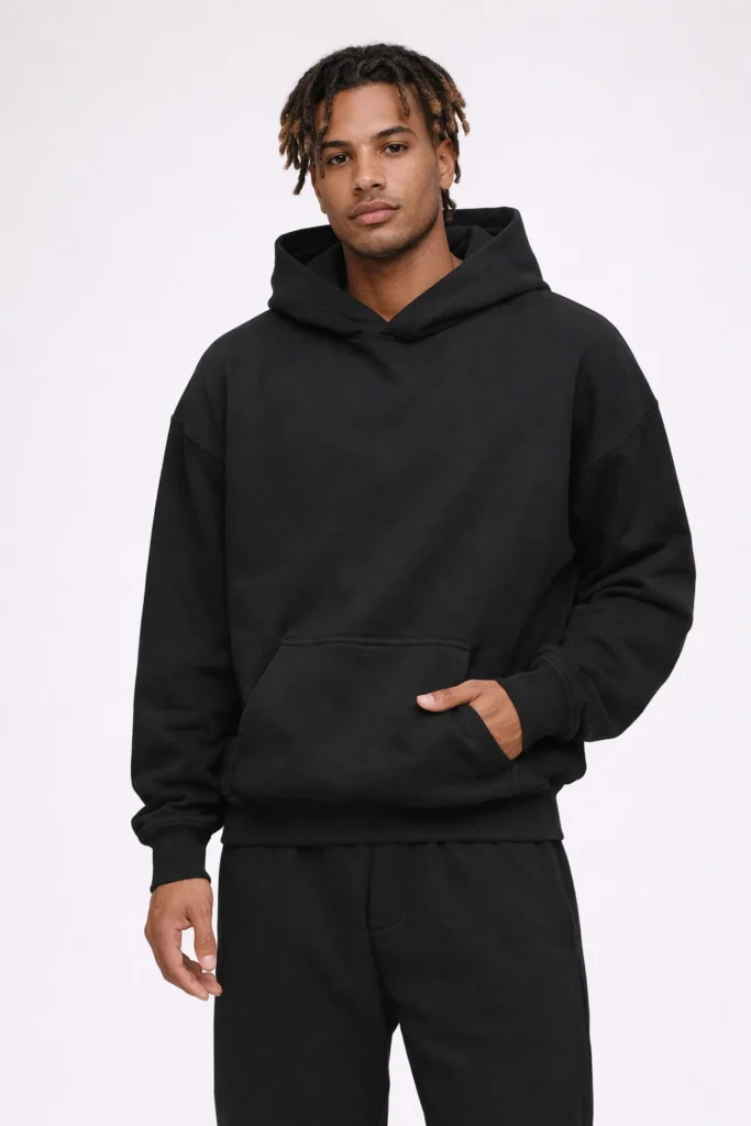 A studio product image showcasing a minimalist black hoodie paired with matching jogger pants. The hoodie features a relaxed fit with a structured hood, ribbed cuffs, and a kangaroo pocket, while the joggers offer a tapered silhouette for everyday comfort. This monochrome set is ideal for custom streetwear, private label loungewear, and OEM/ODM programs focused on timeless design, versatility, and scalable core styles for modern apparel brands.