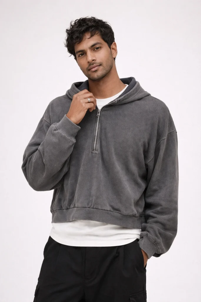 A studio shot featuring a washed grey half-zip hoodie with a relaxed, slightly cropped silhouette. The design includes a metal half-zip neckline, dropped shoulders, ribbed hem and cuffs, and a soft vintage-washed finish. Styled with a white inner tee and black pants, this hoodie is ideal for custom streetwear lines, private label collections, and OEM/ODM programs focused on washed fabrics, modern layering pieces, and elevated casual essentials.