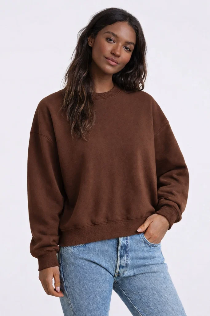 A studio-style image featuring a women’s brown crewneck sweatshirt with a relaxed, effortless silhouette. Made from soft cotton fleece, this sweatshirt is designed with dropped shoulders, ribbed cuffs, collar, and hem for a comfortable everyday fit. Paired with light-wash denim for a clean casual look, it’s ideal for streetwear, lifestyle, and private label collections looking for a warm, neutral-toned essential with broad seasonal appeal.