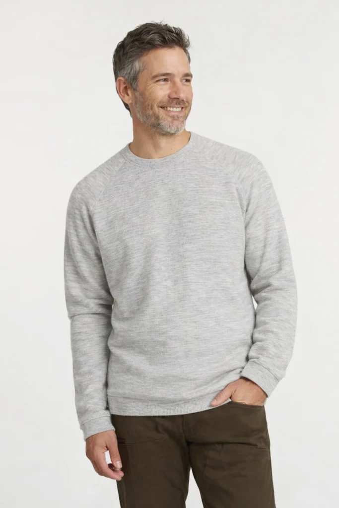 A clean studio image showcasing a men’s light grey crewneck sweatshirt with a minimalist, timeless design. Made from a soft knit fabric, this sweatshirt features a classic round neckline, subtle raglan-style shoulder seams, and ribbed cuffs and hem for a comfortable, structured fit. Styled with casual trousers, it delivers a versatile everyday look ideal for casual wear, lifestyle collections, and private label brands focused on comfort, durability, and understated style.