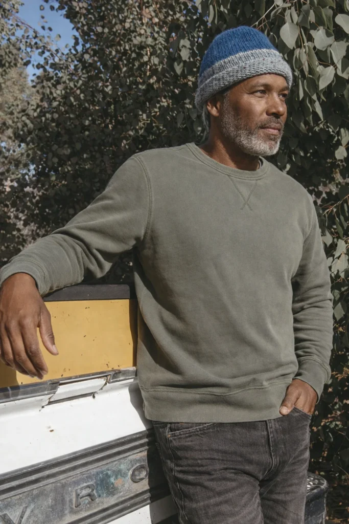 An authentic outdoor lifestyle image featuring a men’s olive green crewneck sweatshirt styled for everyday comfort and versatility. The sweatshirt highlights a classic round neckline, relaxed silhouette, and ribbed cuffs and hem, delivering a timeless and practical design. Paired with dark denim and styled in a natural outdoor setting, this look conveys durability, maturity, and effortless casual appeal—ideal for lifestyle brands, custom apparel collections, and private label sweatshirts designed for year-round wear and laid-back styling.