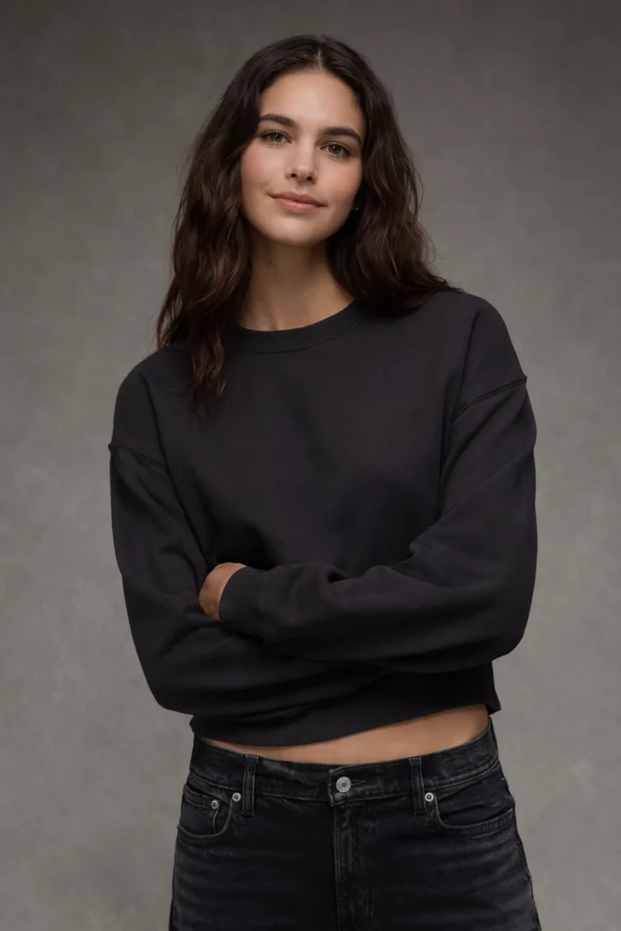 A refined studio portrait featuring a women’s black cropped crewneck sweatshirt with a clean, minimalist silhouette. Designed with a classic round neckline, dropped shoulders, and ribbed cuffs and hem, this piece offers a contemporary cropped fit that balances comfort and modern streetwear appeal. Styled with black denim for a cohesive look, it’s ideal for premium basics collections, private label streetwear brands, and custom apparel lines focusing on versatile, trend-driven essentials with a timeless edge.